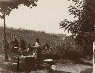 [Deux femmes, l'une assise, l'autre debout rinçant un seau dans un bassin] / [non identifié]. 1910