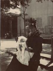 [Femme assise sur un banc tenant dans les bras un bébé en robe de baptême] / [non identifié. [s.n.], [Entre 1903 et 1905]. [1903]-[1905]